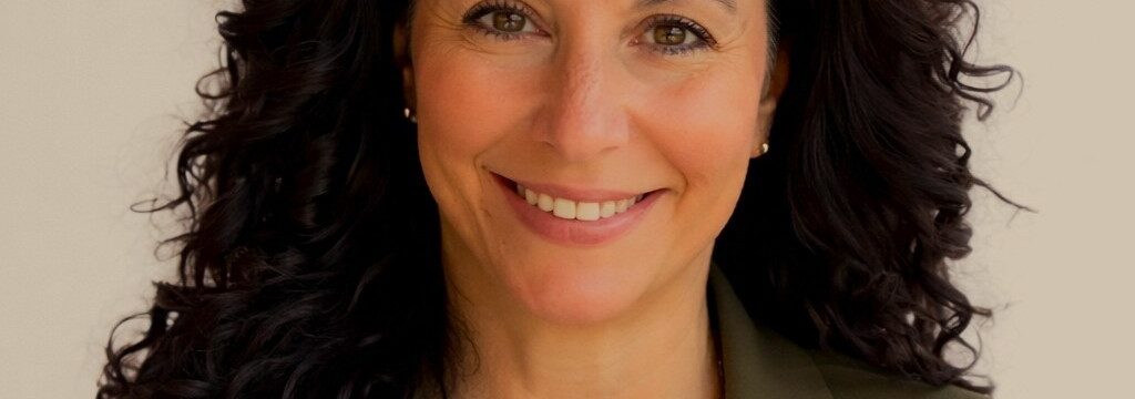 Rosella Hutchison's headshot. She is wearing a white shirt and an olive green blazer