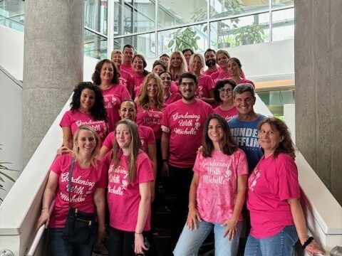 Group of Simpson & McCrady employees stand with volunteers on Phipps Conservatory staircase wearing pink t-shirts