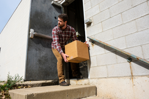 Fidelity & Crime Insurance - Picture of a male warehouse worker leaving a box of merchandise outside of the warehouse for a criminal associate to pick up and steal.