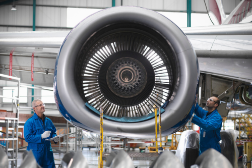 Two engineers or workers working on a jet engine. It is representative of Simpson McCrady offering aerospace insurance.