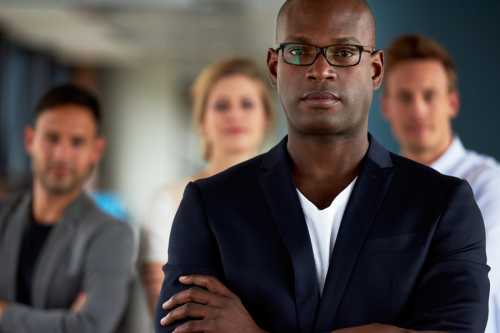 An African executive with his fellow company officers and board directors behind him. Simpson McCrady offers directors and officers liability insurance.