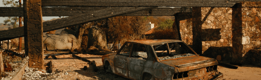 The remains of a high-end home completely destroyed by wildfire in California, with the charred shell of a car and large wooden beams which have been reduced to charcoal. Simpson McCrady Protecting High-Net-Worth Assets in an Evolving Risk Landscape: 2025 Trends.