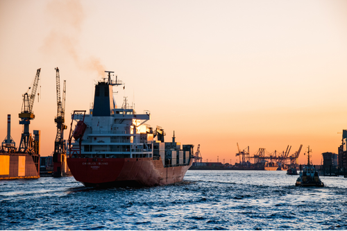 Ocean cargo ship leaving a shipyard at daybreak. Simpson McCrady Ocean Marine Insurance.