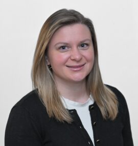 Cora Saftner headshot, wearing white shirt and black sweater, white background