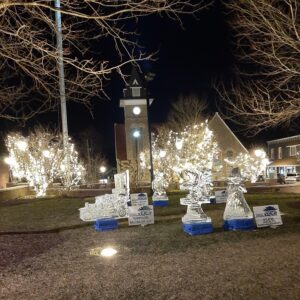 Ice sculptures on grass at night, with a clock tower lit up in the background